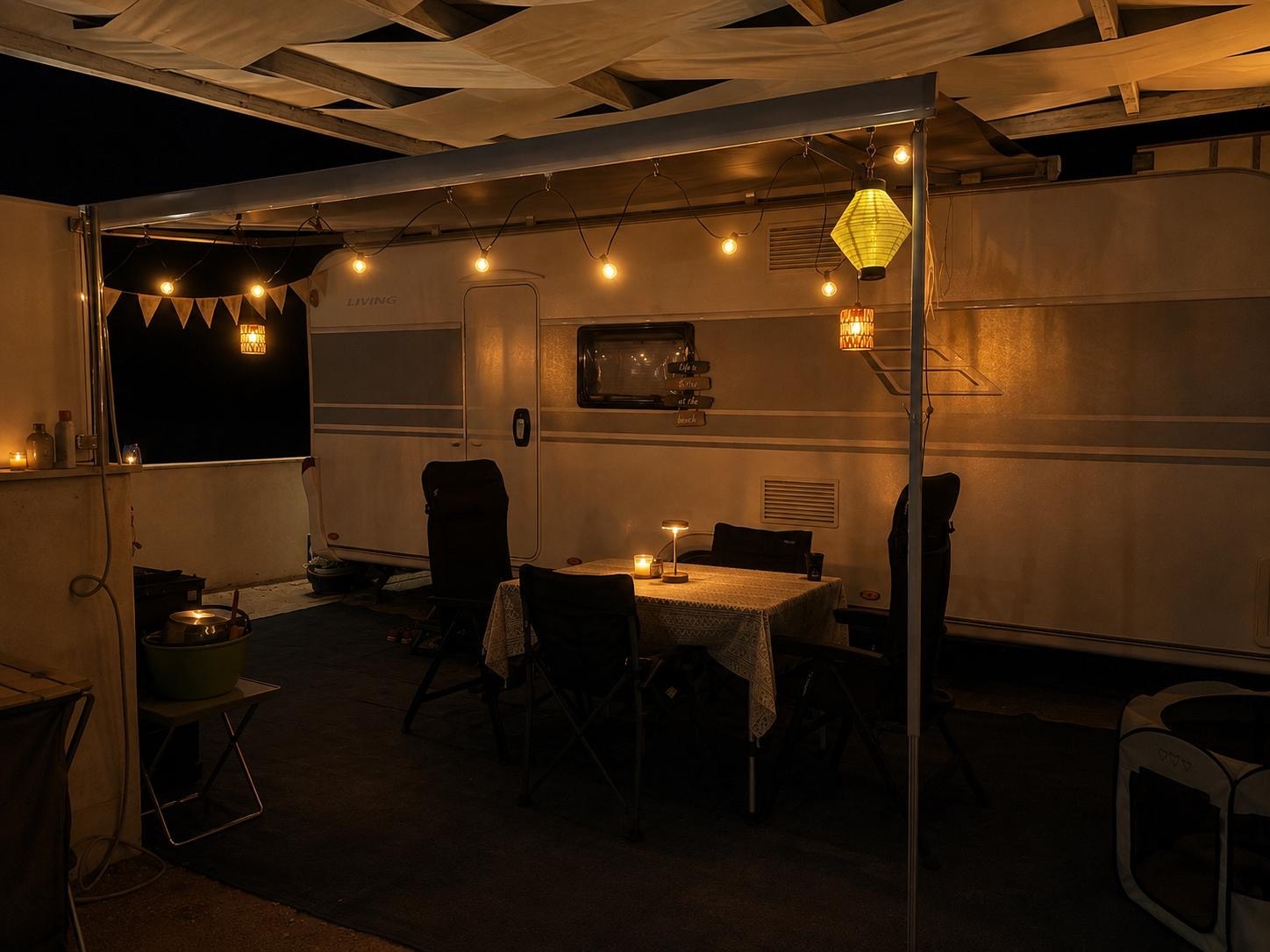 Wohnwagen am Abend mit Lichterkette und warm beleuchtetem Sitzplatz unter der Markise